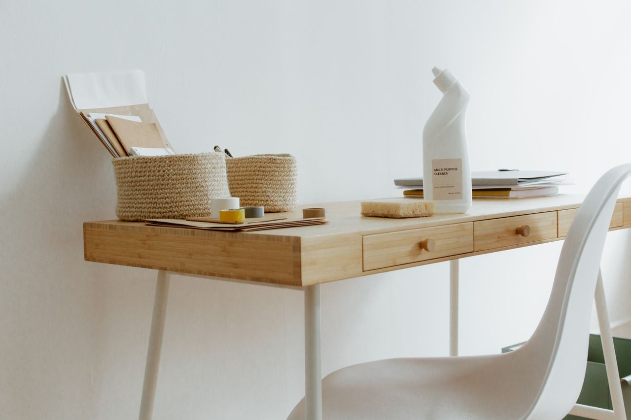 Un bureau de home office propre et bien rangé, avec des produits de nettoyage, des papiers et des paniers de rangement.