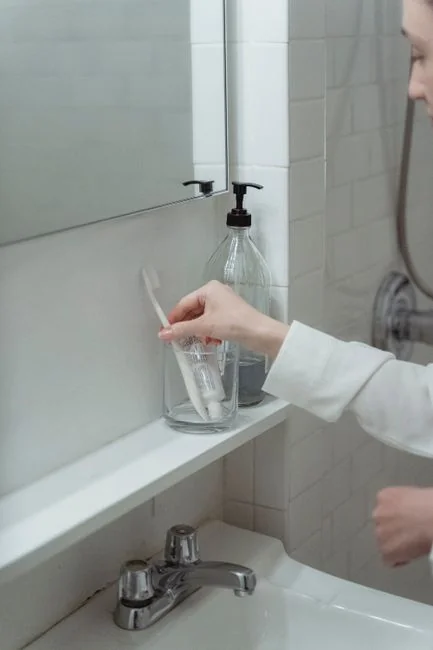 Close-up of hands in yellow gloves cleaning a wall with a spray bottle and sponge.